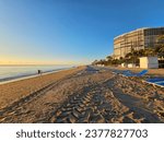 a stunning summer landscape along the beach at sunrise with blue and white lounge chairs, blue ocean water, palm trees, hotels, and footprints in the sand at Bal Harbour Beach in Miami Beach Florida