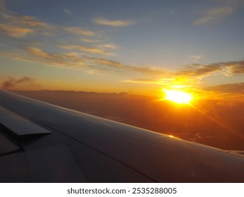 A stunning sunrise from an airplane window shows golden hues above the clouds, with the wing in view, evoking travel, adventure, and the beauty of flight—perfect for wanderlust themes. - Powered by Shutterstock