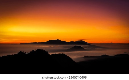 A stunning sunrise over the mountains, with dark peaks rising above a sea of clouds. The sky shifts from yellow to orange, contrasting beautifully with the silhouetted mountains and soft clouds below. - Powered by Shutterstock