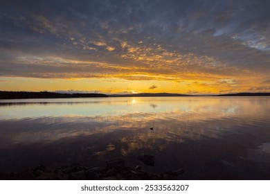 A stunning sunset over a calm lake with vibrant orange and blue hues reflecting in the water, surrounded by distant hills. - Powered by Shutterstock