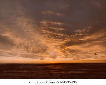 A stunning sunset over the ocean with dramatic golden and orange tones filling the sky. The horizon glows warmly as the sun sets, while textured clouds create a beautiful and atmospheric seascape. Perfect for themes of nature, calm, travel, and serenity.