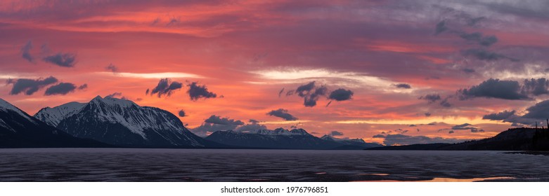 Stunning sunset over snow capped mountain peaks in northern Canada during spring time with purple, peach and pink colors in natural, wild setting. Taken in Warm Bay, Atlin, British Columbia, Canada. 