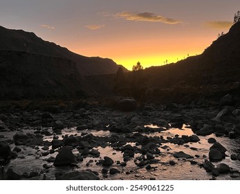 Stunning sunset over a tranquil river with rocky shores, framed by dark silhouettes of the Andes mountains in Peru. - Powered by Shutterstock