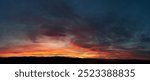 Stunning sunset paints sky with vibrant hues of red, orange, and pink, blending into deep blues and purples. Silhouetted hills create contrast against fiery horizon, adding drama to serene landscape.