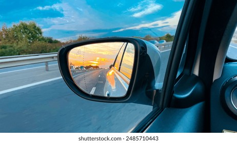 A stunning sunset reflected in the side mirror of a car, capturing the beauty of the open road and the sky’s vivid colors.
