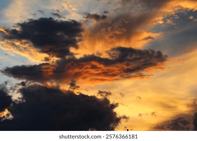 A stunning sunset sky with dramatic dark clouds illuminated by vibrant orange and yellow hues, creating a captivating and serene atmosphere