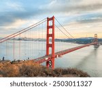 A stunning sunset view of the Golden Gate Bridge facing toward San Francisco. The iconic landmark is beautifully silhouetted against the evening sky, vibrant sunset colors and the city