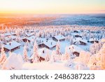 Stunning sunset view over wooden huts and snow covered trees in Finnish Lapland