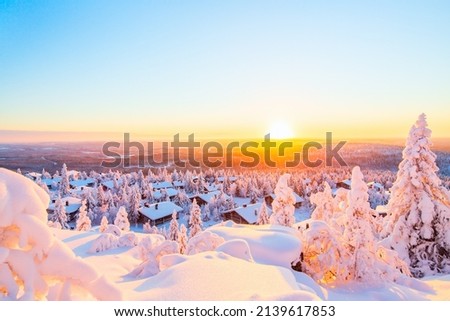 Stunning sunset view over wooden huts and snow covered trees in Finnish Lapland