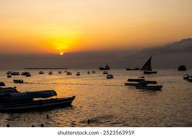 A stunning sunset in Zanzibar, where the sky is painted with vibrant shades of orange and purple. Traditional boats glide gracefully across the shimmering waters - Powered by Shutterstock