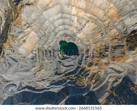 A stunning top-down drone view of a massive open-pit mine, showcasing its terraced layers and a vibrant turquoise lake at its center