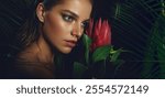 Stunning tropical beauty portrait featuring a glamorous woman holding a vibrant red protea flower, set against lush jungle leaves. Perfect for fashion editorials, nature themes, or exotic beauty.