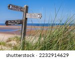 Stunning view across Burnham Overy Staithe beach, with tropical blue seas, part of the Norfolk Coast Path with Coastal Path signpost within the dunes pointing towards Holkham and Burnham Overy Staithe