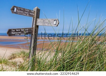 Stunning view across Burnham Overy Staithe beach, with tropical blue seas, part of the Norfolk Coast Path with Coastal Path signpost within the dunes pointing towards Holkham and Burnham Overy Staithe