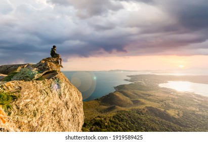 Stunning view of a boy enjoying a beautiful sunset sitting on top of a mountain, Golfo Aranci, Sardinia, Italy.