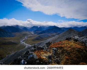 A stunning view of the Brooks Range and its distant peaks from a rocky hilltop, offering a breathtaking perspective of the Alaskan wilderness.