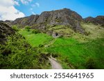 A stunning view of Cave Hill near Belfast, Northern Ireland, featuring a hiking trail winding through vibrant green grass towards a natural cave entrance on the rugged hillside. This scenic landscape 