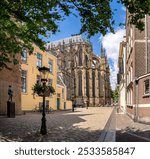 A stunning view of the Dom Tower in Utrecht, Netherlands, framed by historic buildings and lush green trees on a sunny day.