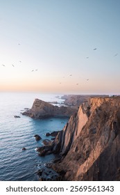 A stunning view of the dramatic cliffs in Sagres, Portugal, where rugged rock formations meet the vast Atlantic Ocean.
