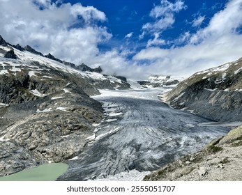 A stunning view of a glacier surrounded by rocky terrain and alpine peaks under a cloudy sky. - Powered by Shutterstock