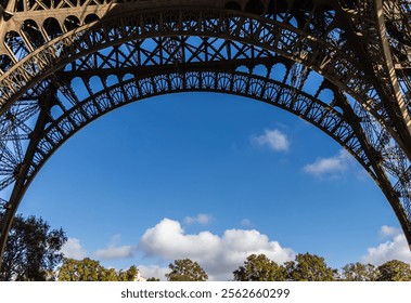 A stunning view of the iconic Eiffel Tower arch set against a serene blue sky with fluffy white clouds floating by