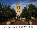 A stunning view of the iconic Memorial Union Tower at the University of Missouri, framed by lush greenery and flower beds on a clear day.