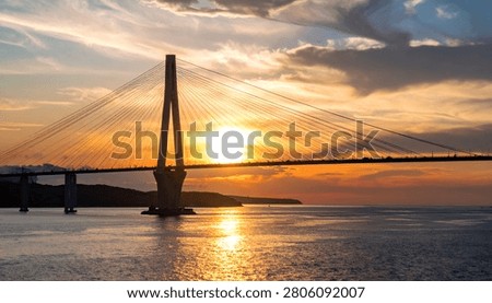 A stunning view of a modern cable-stayed bridge at sunset, with the sun casting a golden glow on the water and sky.