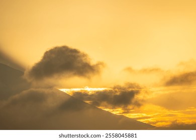 A stunning view of Mount Fuji silhouetted against a golden sunset, with dramatic clouds partially covering the iconic peak.  - Powered by Shutterstock