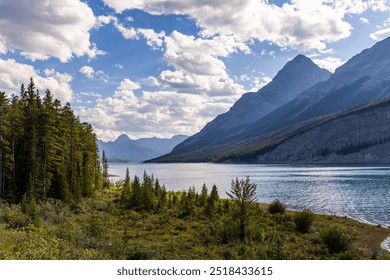 A stunning view of the mountain landscape in Kananaskis, Alberta, Canada featuring a tranquil lake, dense forest, and vibrant blue sky. - Powered by Shutterstock