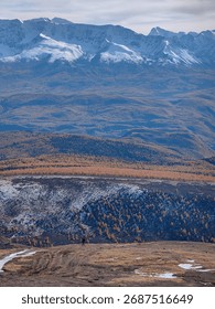 A stunning view of a mountain range with snow-capped peaks and a person standing on a hill.