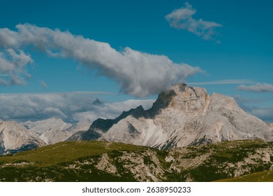 A stunning view of a mountain range under a clear blue sky with a cloud hovering over the peak.