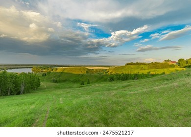 A stunning view of a river valley from a grassy hillside, with lush greenery, fluffy clouds, and a tranquil blue sky. The scene captures the beauty of a spring evening. - Powered by Shutterstock