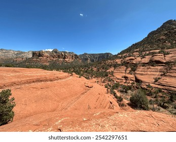 Stunning view of Sedona's iconic red rock formations under a clear blue sky. Rugged desert terrain with rocky outcrops and sparse vegetation in a picturesque arid landscape. - Powered by Shutterstock