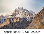 A stunning view of sharp, jagged mountain peaks partially covered by clouds, with golden sunlight casting a warm glow on the rocky cliffs, creating a dramatic and awe-inspiring landscape.