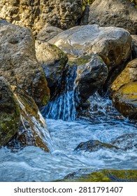  A stunning view of a small waterfall cascading over textured rocks into a river, highlighting the refreshing, clear water and the serene atmosphere of a mountain forest landscape.