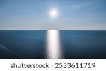 A stunning view of the sun shining over a calm ocean with a clear blue sky.