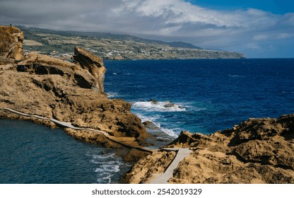 A stunning view of towering coastal cliffs carved by the relentless force of ocean waves, creating deep crevices where the blue water crashes between the rock formations. - Powered by Shutterstock