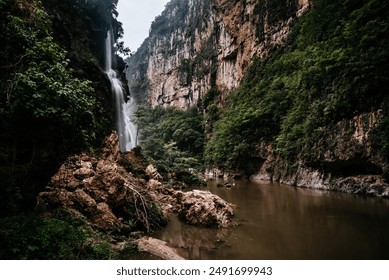 A stunning view of a waterfall cascading down towering cliffs into the serene waters of the Grijalva River in Mexico. The dramatic landscape is surrounded by lush greenery, capturing the essence. - Powered by Shutterstock