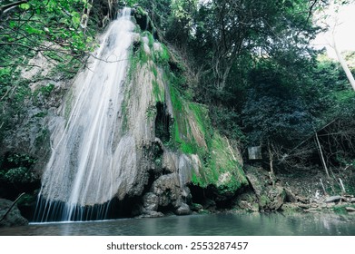 A stunning waterfall cascades down rocky cliffs, enveloped by vibrant greenery and surrounded by a tranquil pool. A perfect capture of nature's beauty. - Powered by Shutterstock