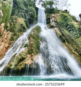 A stunning waterfall cascading down moss-covered rocks into a clear turquoise pool, surrounded by lush greenery. Perfect for nature and travel themes.Minas viejas Huasteca potosina