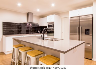 A Stunning White Modern Kitchen With Stone Bench Tops And Wooden Flooring