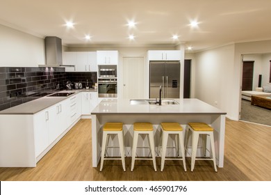 A Stunning White Modern Kitchen With Stone Bench Tops And Wooden Flooring