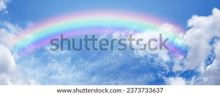 Stunning wide blue sky and bright rainbow - big fluffy clouds with a giant arcing rainbow against a beautiful summer time blue sky with copy space for positive spiritual messages
