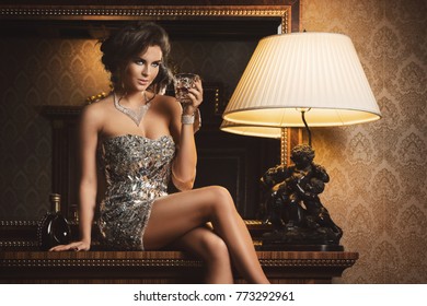 Stunning woman wearing beautiful shiny dress with a glass of cognac