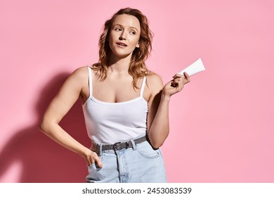 A stunning woman in a white tank top gracefully poses while holding cream. - Powered by Shutterstock