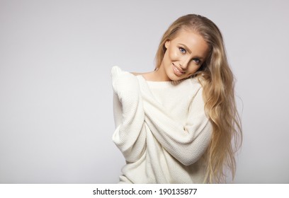 Stunning Young Female Fashion Model With Long Hair Posing In Oversized Sweater. Young Blond Woman Posing On Grey Background