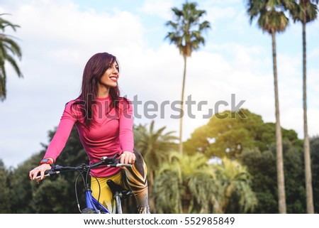 Stunning young woman in her sports outfit on a bicycle in a beautiful exotic tropical park - Beautiful smiling woman enjoying outdoor activities admiring the view