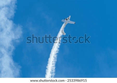 Stunt aerobatic plane performing loop in blue sky with smoke trail. Concept of speed, difficulty, precision, risk, challenge