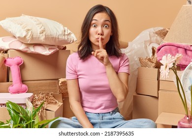 Stupefied Asian Woman Makes Silence Gesture Presses Index Finger Over Lips Dressed In Pink T Shirt And Jeans Relocates To New Apartment Packs Personal Belongings In Boxes. Ownership Of Property