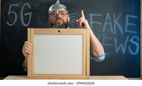 Stupid Conspiracy Theory Guy In A Foil Hat Holds A Blackboard With Space For Text. A Bearded Conspiracy Theorist. Total Control And Fake News. Conspiracy And 5g. Mind Control. Thumbs Up Onto The Board